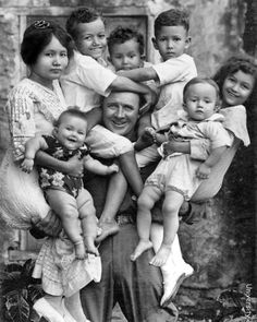 an old black and white photo of a man with six children in his arms, posing for the camera