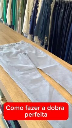 the pants are lined up on the table in front of some other clothes hanging from racks