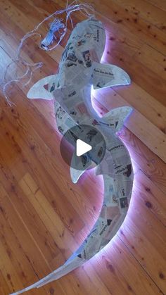 a sculpture made out of newspaper strips on a wooden floor with a light coming from it