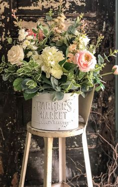 a white bucket filled with flowers sitting on top of a stool