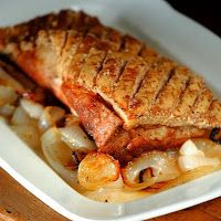 a piece of fish sitting on top of onions in a white dish next to a knife and fork