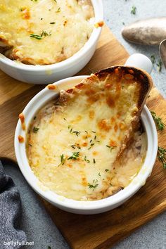 two white bowls filled with cheesy potatoes on top of a wooden cutting board