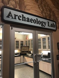 the entrance to an archaeolgy lab with glass doors and black lettering on it