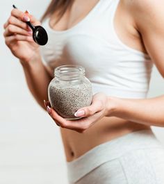 a woman holding a jar filled with sand and a black object in her hand,