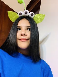 a woman with long black hair wearing a blue shirt and green leaves on her head