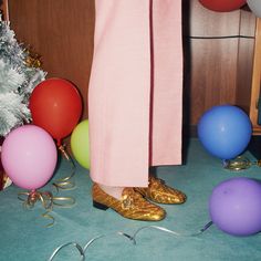 a person wearing gold shoes standing in front of balloons and streamers on the floor