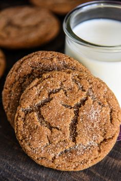 two cookies and a glass of milk on a wooden table with other cookies in the background