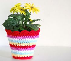 a crocheted flower pot with yellow flowers in it on a table next to a white wall