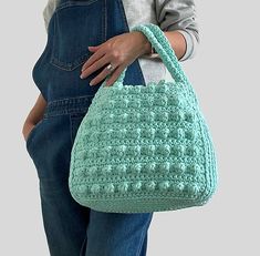 a woman is holding a crocheted bag in her hands and wearing overalls