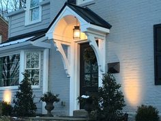 a white house with black shutters and lights on it's front door at night