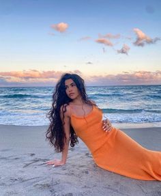 a woman in an orange dress sitting on the beach