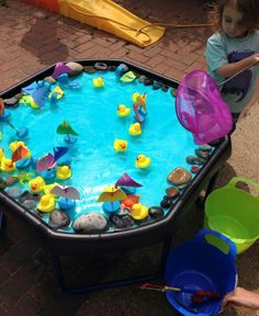 two children playing with toys in an outdoor play pool on the ground next to water