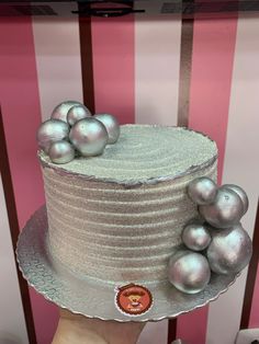 a hand holding a cake decorated with silver balls