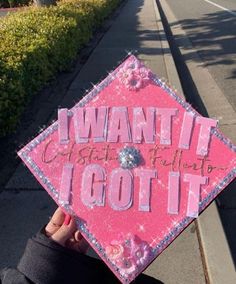 someone holding up a pink graduation cap that says i want it got it