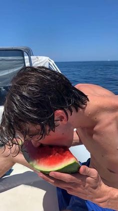 a man is eating a piece of watermelon on a boat in the ocean