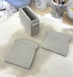 two gray square shaped dishes sitting on top of a table next to cups and pencils