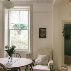 a room with a table, chairs and a vase of flowers on the window sill