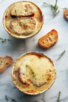 two bowls filled with food sitting on top of a marble counter next to slices of bread