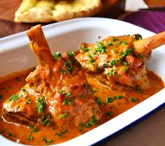 a white plate topped with meat covered in sauce and garnished with parsley