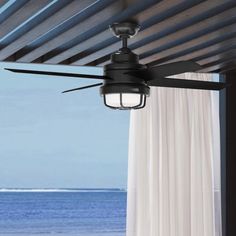 a ceiling fan with a light hanging from it's side next to a window overlooking the ocean