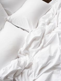 an unmade bed with white sheets and pillows