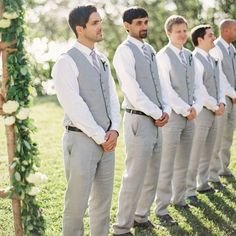 a group of men standing next to each other in front of a wooden arch with flowers on it