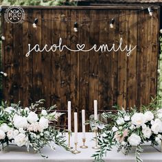 a table with candles, flowers and greenery is set up in front of a wooden wall