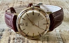 This vintage Smiths Jewelled handwind shockproof watch is a true gem for any watch collector. With a gold-plated case and brown leather strap, this classic round watch boasts an ivory dial with Arabic numerals and baton indexes. The watch is designed for men and has a maximum wrist size of 21.1-22 cm, with a lug width of 18 mm and a case thickness of 10 mm. The watch features a mechanical (manual) movement and a 12-hour dial, along with shock-resistant capabilities. It comes without papers, serv Antique Brown Analog Watch, Vintage Brown Watch For Anniversary, Vintage Brown Watch Accessories For Anniversary, Retro Brown Watch For Anniversary, Retro Brown Watch Accessories With Chronometer, Round Watch, Brown Leather Strap, Wristwatch Men, Watch Collection