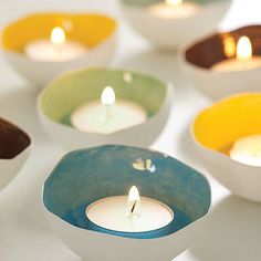 several bowls with lit candles in them sitting on a white counter top, one is blue and the other is yellow