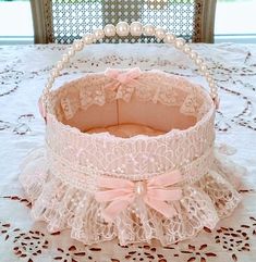 a white lace basket with pink ribbon and pearls on the top is sitting on a table