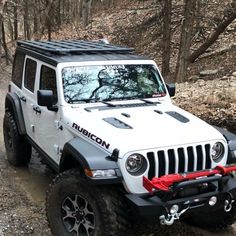 a white jeep driving down a trail in the woods