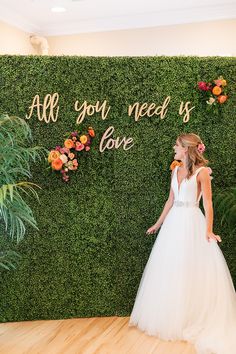 a woman standing in front of a green wall with flowers on it and the words all you need is love