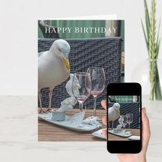 a person holding up a card with a seagull and wine glasses on it