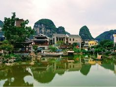 a river surrounded by buildings and trees in the middle of a town with mountains behind it