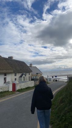 a woman is walking down the road towards some houses by the ocean with a thatched roof