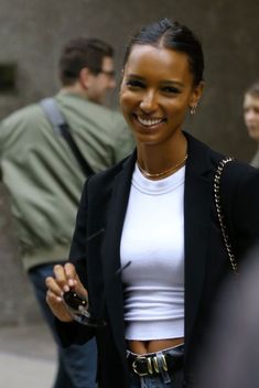 a woman in white shirt and black blazer smiling at the camera with other people behind her