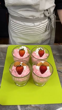 four desserts with strawberries and whipped cream in small bowls on a green mat