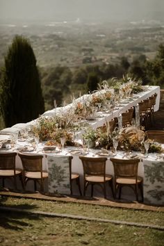 a long table is set up with flowers and greenery for an outdoor wedding reception