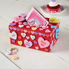 a red box with hearts on it sitting on the floor next to a cupcake