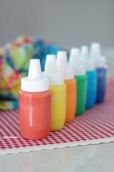 there are many different colors of paint in bottles on the tablecloth next to an orange bowl