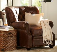 a living room with a brown leather chair and white throw pillows on the floor next to a wicker basket