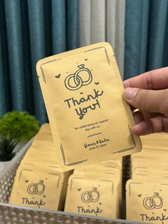 a person holding up a thank you card in front of some boxes with wedding rings on them