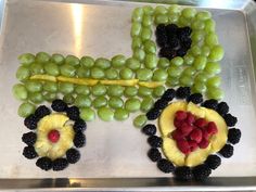 a metal tray topped with grapes, fruit and a tractor shaped like a train on top of it