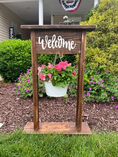 a welcome sign with potted flowers in front of a house on the grass and bushes