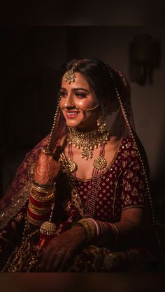 a woman in a red and gold bridal outfit smiles while holding her hand up to her face