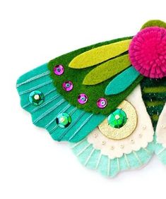 a green and pink butterfly brooch sitting on top of a white surface