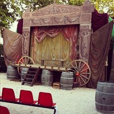 an outdoor stage set with red chairs and barrels in the foreground, behind which is a wooden wagon