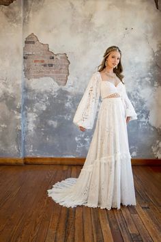 a woman in a white dress standing on a wooden floor with an old wall behind her