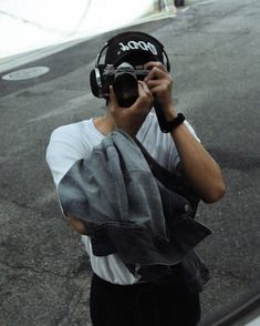 a man wearing headphones and holding a camera up to his face while standing on the street