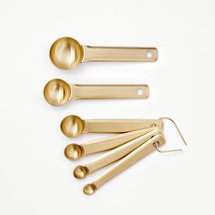 four golden measuring spoons and two ladles on a white surface